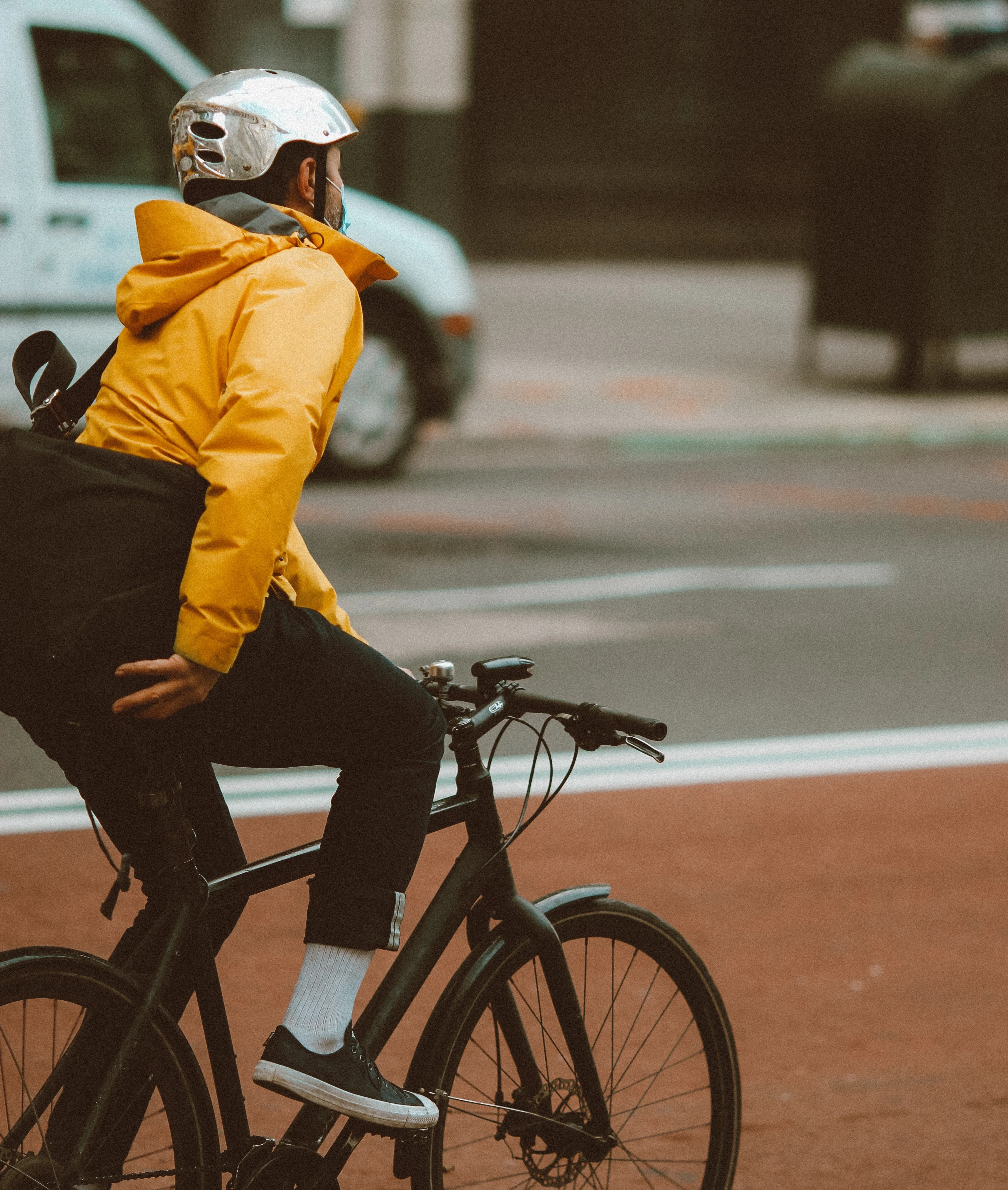 Salarié en veste jaune et casque blanc qui roule à vélo en ville, sac sur le dos.