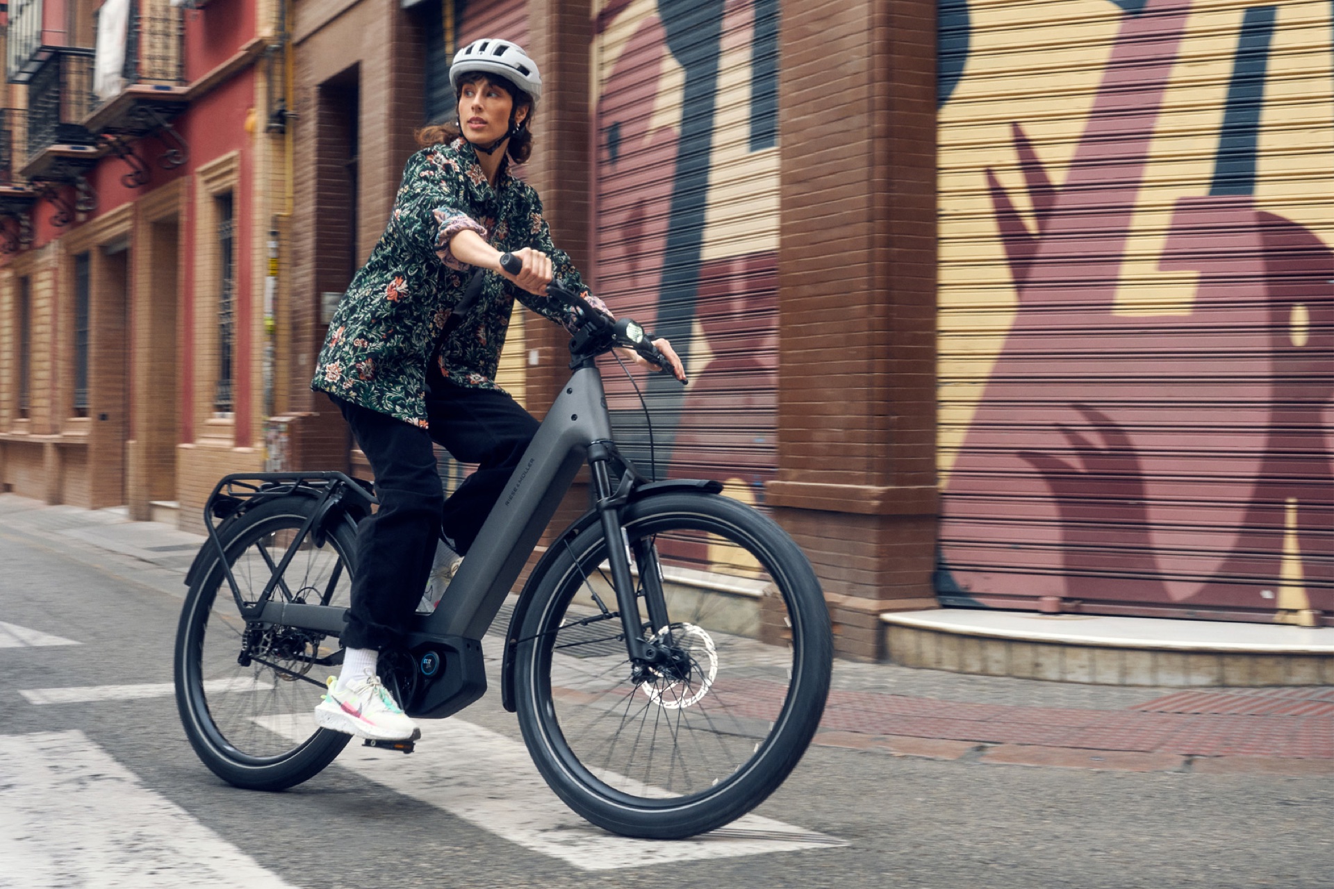 Cycliste casquée sur un vélo de ville électrique Riese & Müller, dans une rue aux rideaux de fer peints.