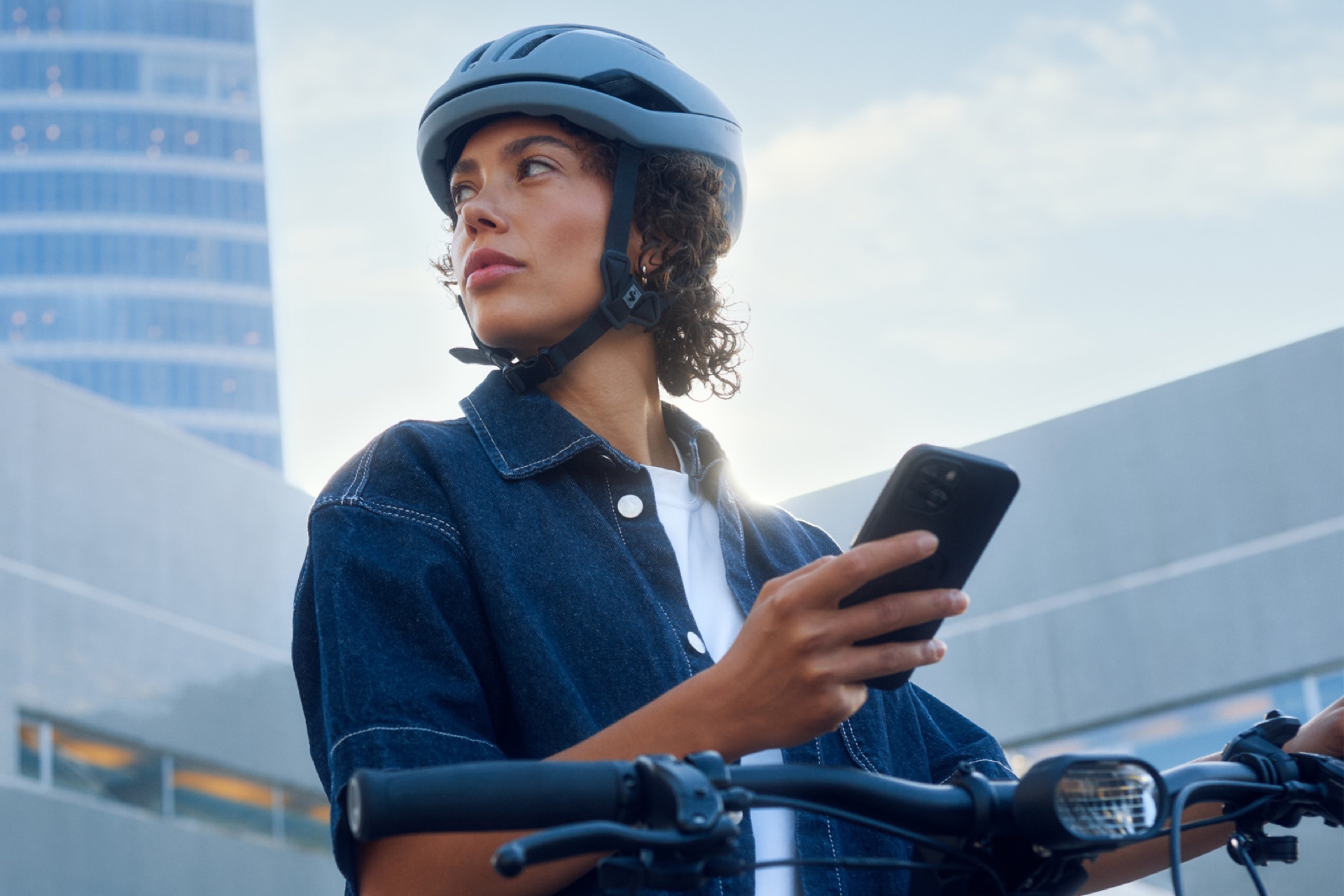 Cycliste casquée qui consulte son téléphone avant de partir, au pied des immeubles de bureaux.